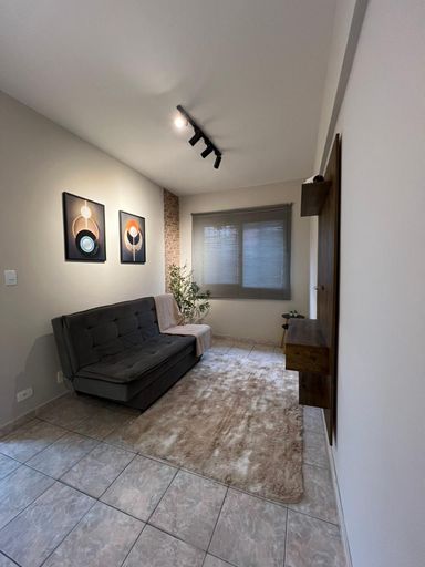 Sala bem iluminada com janela grande, sofá cama e painel de TV.