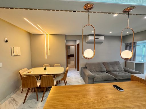 Sala de dois ambientes, com sofá, mesa de jantar para seis pessoas, iluminação em LED e piso em porcelanato.