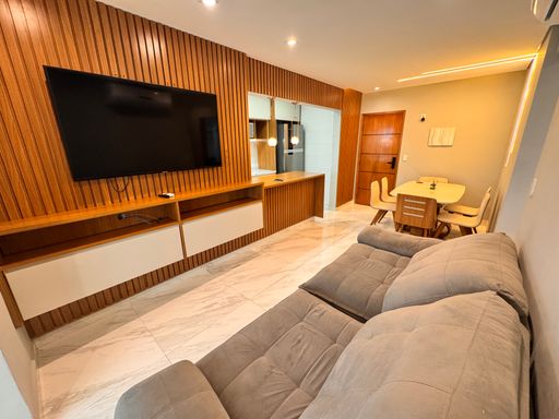 Sala de dois ambientes, com painel ripado, sofá, mesa de jantar para seis pessoas, iluminação em LED e piso em porcelanato.