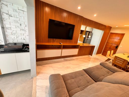 Sala de dois ambientes, com painel ripado, sofá, mesa de jantar para seis pessoas, iluminação em LED e piso em porcelanato.