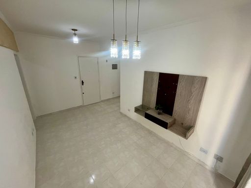 Sala espaçosa com paredes brancas, painel de TV e uma sacada.