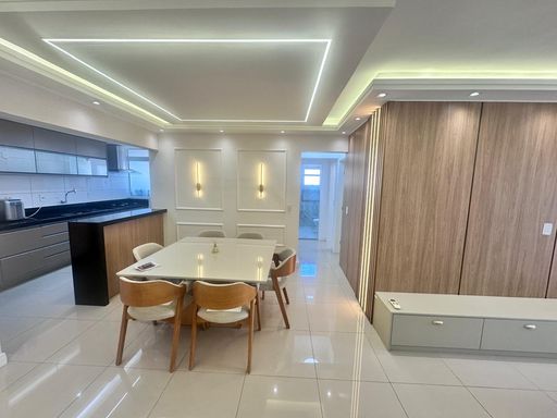 Sala de dois ambientes com sofá novo, mesa com seis cadeiras, painel com rack e LED, boiserie com arandela e teto rebaixado em gesso com iluminação em LED.