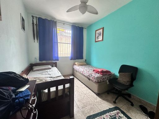 Dormitório com duas camas de solteiro, ventilador de teto, uma janela grande, uma parede azul e outra branca.