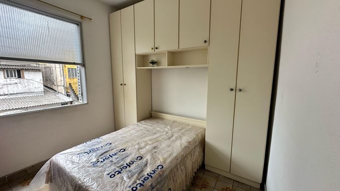 Sala living bem iluminada com uma cama de casal e armários brancos.