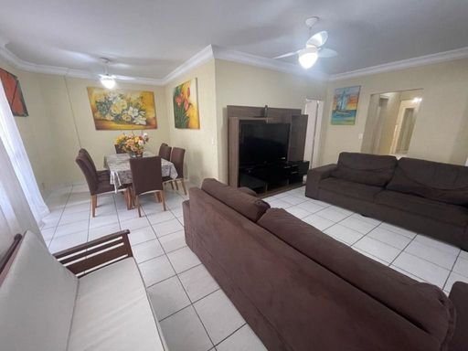 Sala ampla de dois ambientes com três sofás, mesa de jantar para oito pessoas e ventilador de teto.