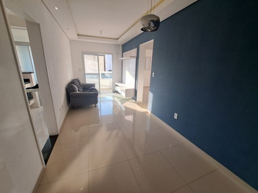 Sala de dois ambientes com muita iluminação natural, uma parede azul e outra branca, com sofá e painel de TV.