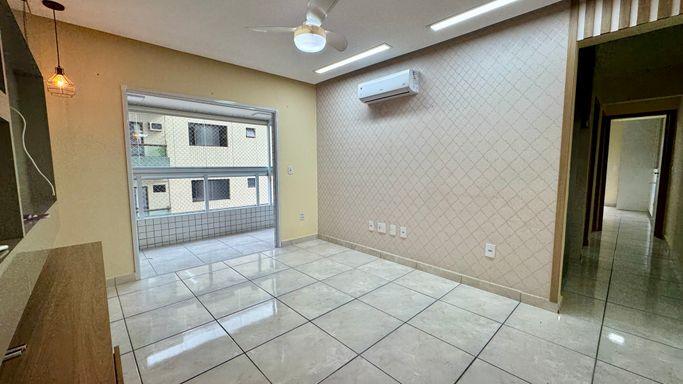 Sala espaçosa e bem iluminada com painel de TV, ventilador de teto e ar-condicionado.