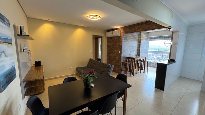 Sala de 2 ambientes com uma mesa de jantar, sofá cama e painel de TV.