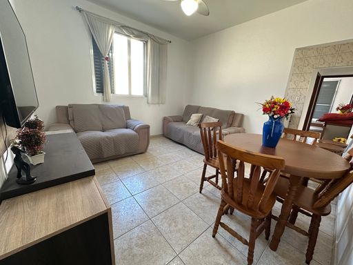 Sala bem iluminada com dois sofás, mesa de jantar, rack, TV e ventilador de teto.