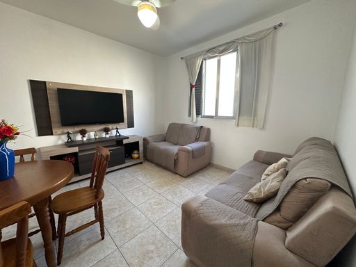Sala bem iluminada com dois sofás, mesa de jantar, rack, TV e ventilador de teto.