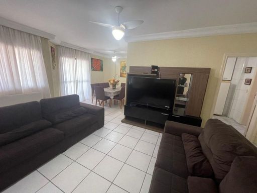 Sala ampla de dois ambientes com três sofás, mesa de jantar para oito pessoas e ventilador de teto.