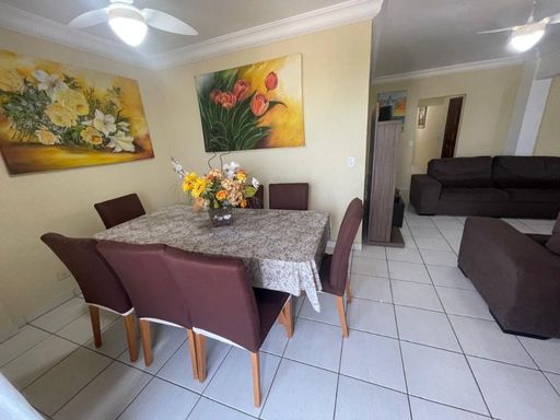 Sala ampla de dois ambientes com três sofás, mesa de jantar para oito pessoas e ventilador de teto.