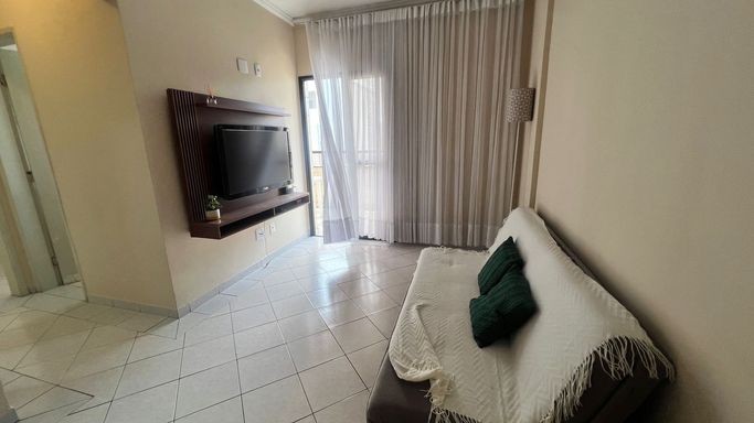 Sala de 2 ambientes com sofá, painel de TV, mesa de jantar e acesso a sacada.