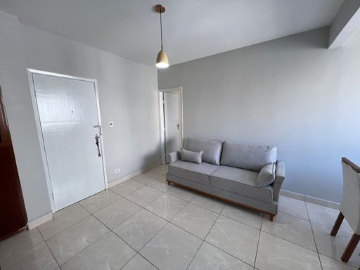 Sala bem iluminada com sofá cinza, mesa de jantar e painel de TV.