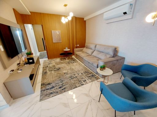 Sala de 2 ambientes com muita iluminação natural, sofá de dois lugares, lustre pendente e ar-condicionado.