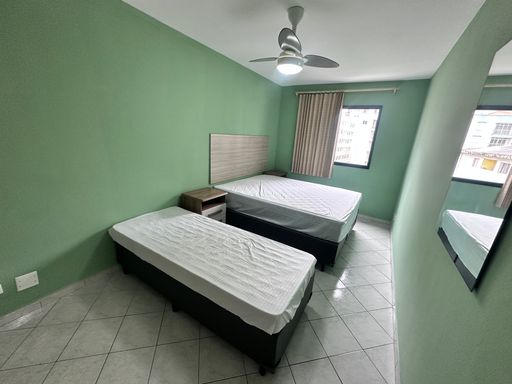 Dormitório bem iluminado, com paredes verdes, cama de casal, cama de solteiro, guarda-roupa e ventilador de teto