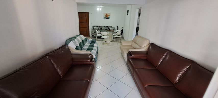 Sala de dois ambientes, com cinco sofás, mesa de jantar e dois ventiladores de teto.
