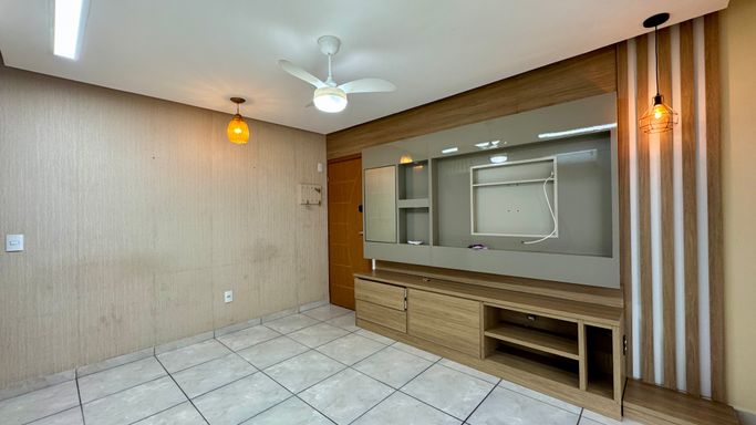 Sala espaçosa e bem iluminada com painel de TV, ventilador de teto e ar-condicionado.