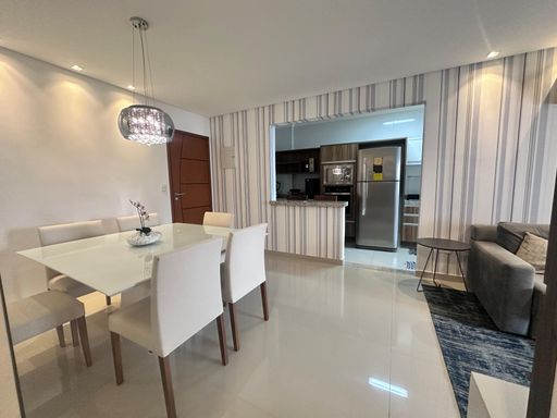 Sala ampla com dois ambientes, com ar-condicionado, sofá, mesa de jantar, parede espelhada e um elegante lustre pendente.