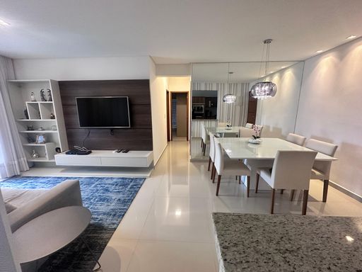 Sala ampla com dois ambientes, com ar-condicionado, sofá, mesa de jantar, parede espelhada e um elegante lustre pendente.