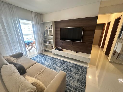 Sala ampla com dois ambientes, com ar-condicionado, sofá, mesa de jantar, parede espelhada e um elegante lustre pendente.