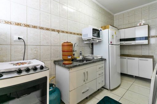 Cozinha com armários brancos, geladeira, pia com gabinete e fogão.