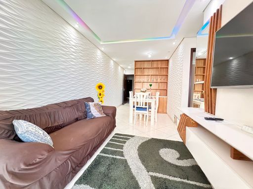 Sala bem iluminada de 2 ambientes com um sofá, painel de TV, teto rebaixado em gesso com iluminação em LED.