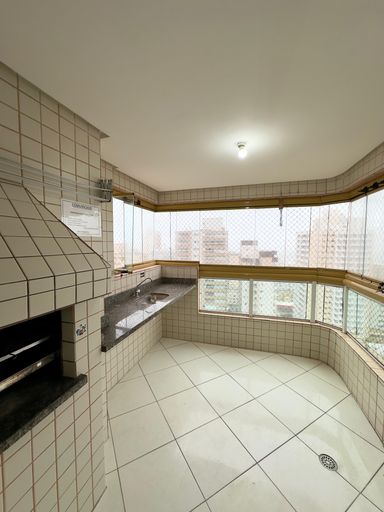 Sacada gourmet com churrasqueira a carvão, envidraçada com vista para o mar.