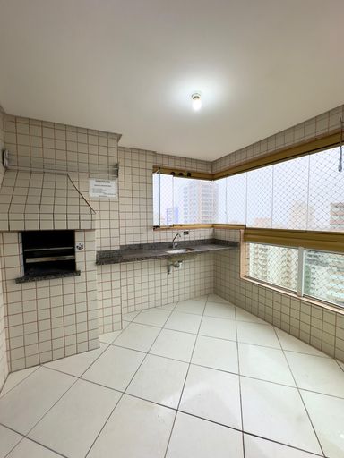 Sacada gourmet com churrasqueira a carvão, envidraçada com vista para o mar.