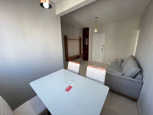 Sala bem iluminada com sofá cinza, mesa de jantar e painel de TV.