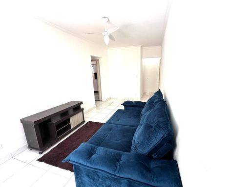 Sala bem iluminada com um sofá azul e ventilador de teto.