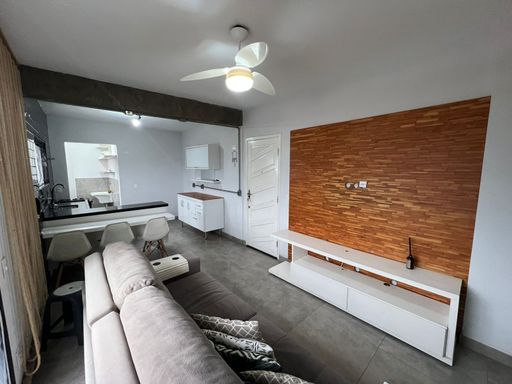 Sala bem iluminada com um sofá cinza, painel de TV e uma sacada.