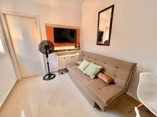Sala bem iluminada com um sofá cama, TV e espelho.