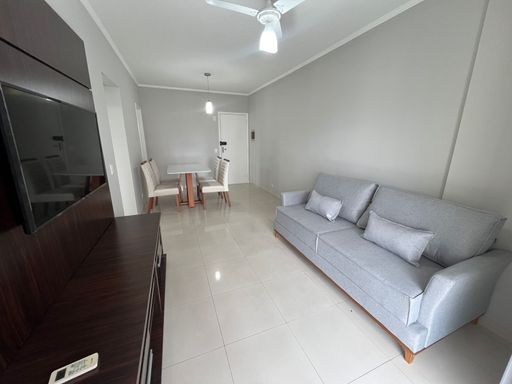 Sala de dois ambientes com mesa de jantar para quatro pessoas, sofá, painel de TV, ar-condicionado e acesso à sacada gourmet.