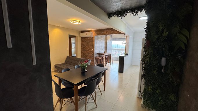 Sala de 2 ambientes com uma mesa de jantar, sofá cama e painel de TV.