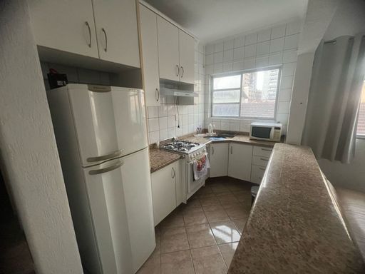 Cozinha americana com armários planejados, geladeira e fogão.