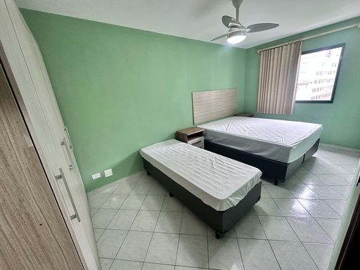 Dormitório bem iluminado, com paredes verdes, cama de casal, cama de solteiro, guarda-roupa e ventilador de teto