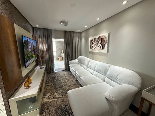 Sala com dois ambientes, sofá branco e acesso à sacada gourmet.