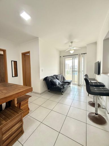 Sala de dois ambientes com mesa de jantar, sofá cama, acesso a sacada gourmet e ventilador de teto.